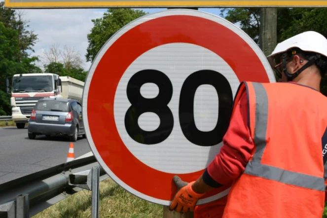 Un employé de la Direction interdépartementale des routes (DIR) installe un panneau de limitation de vitesse à 80 km/h sur une route nationale