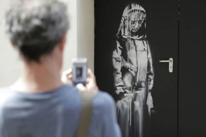 Un passant photographie une oeuvre de Banksy en hommage aux victimes des attentats de 2015 au Bataclan à Paris, le 25 juin 2018.