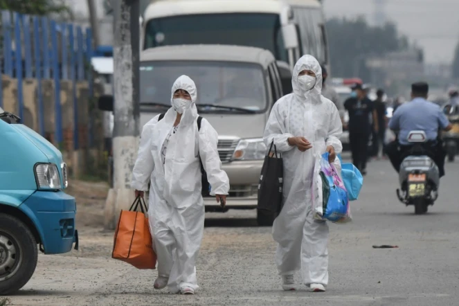 Deux Chinoises en combinaison intégrale de protection passent près du marché de Xinfadi, fermé après l'apparition de nouveaux cas de coronavirus, le 13 juin 2020 à Pékin