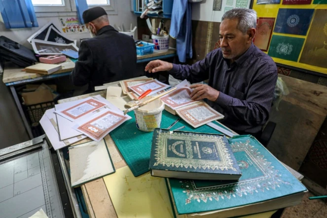 L'artisan Khaled al-Drebi (d) assemble les pages d'un vieux manuscrit dans son atelier où il restaure des Corans anciens ou abîmés, le 22 mars 2022 à Tripoli, en Libye