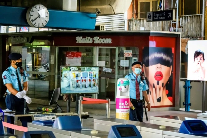 En Thaïlande, des forces de sécurité postées à un point de contrôle des températures, près d'un salon de manucure fermé, à une station du métro de Bankgok le 2 janvier 2021