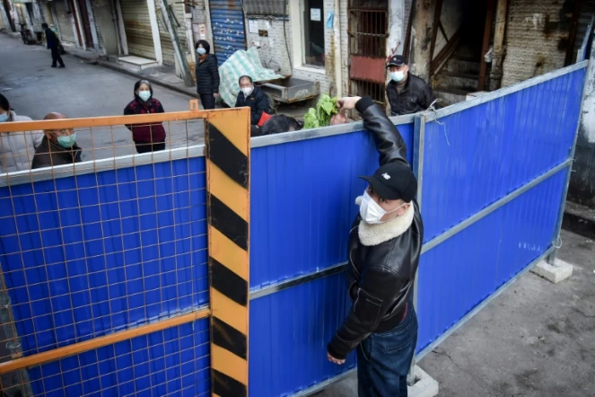 Un homme livre des légumes à une personne derrière une barrière à Wuhan le 24 février 2020