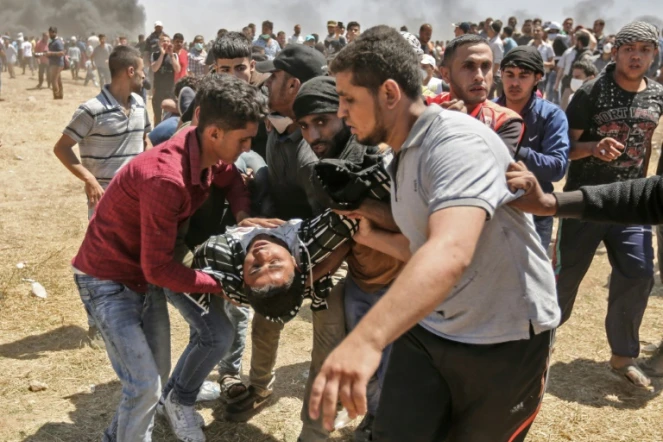Un Palestinien blessé par des tirs israéliens est évacué par d'autres manifestants, le 14 mai 2018 dans la bande de Gaza, à la frontière avec Israël