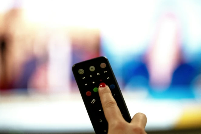 Une personne tient une télécommande pointée vers un écran de télévision, à Paris le 15 janvier 2025