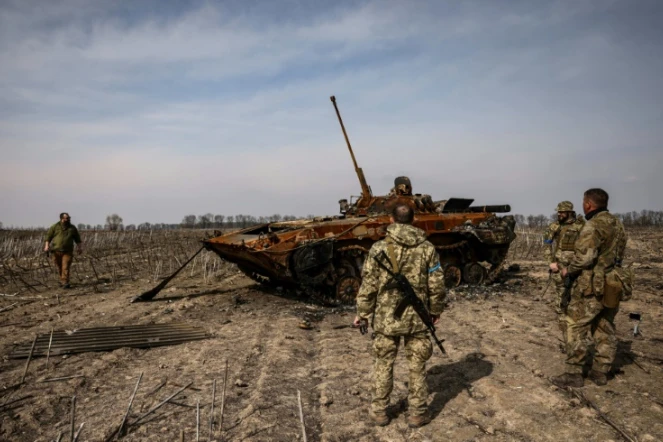 Des soldats ukrainiens se tiennent près d'un tank russe calciné le 31 mars 2022 dans la banlieue de Kiev