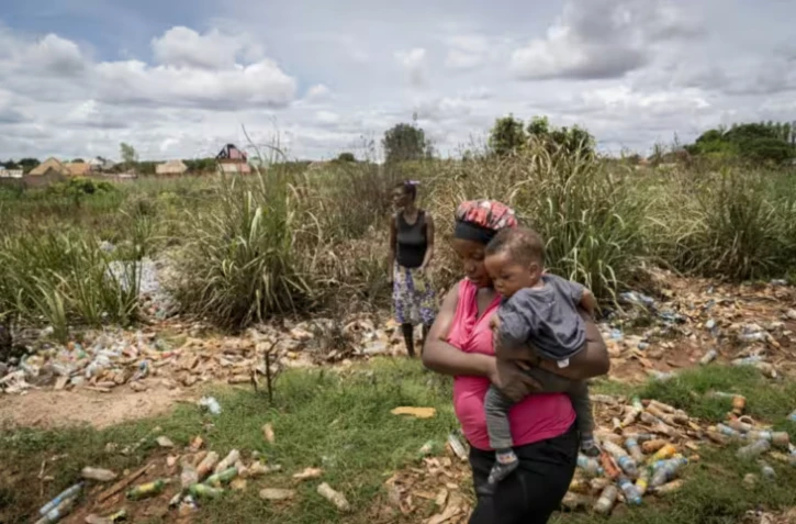 Hélène Mvubu porte sa fille en marchant dans un champ pollué à Lubumbashi en République démocratique du Congo le 24 novembre 2025 ( AFP / Glody MURHABAZI )