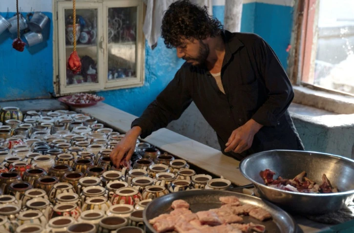 Dans cette photo prise le 14 juin 2023, Waheed, un chef cuisinier afghan propriétaire d’un restaurant à Kaboul, met de la viande dans des théières en préparant un plat traditionnel appelé « chainaki », un ragoût d’agneau