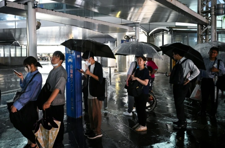 Des personnes attendent un taxi à la station de métro de Chiba, dans la ville de Chiba à l'est de Tokyo, le 13 août 2026, alors que de fortes pluies s'abattent sur la région