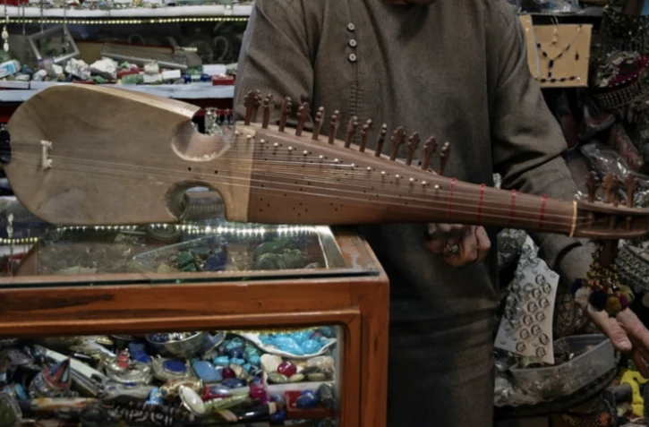 Gull Agha, un joueur amateur afghan de rubab, présente l'instrument dans un magasin à Herat, le 21 décembre 2024 ( AFP / Wakil KOHSAR )