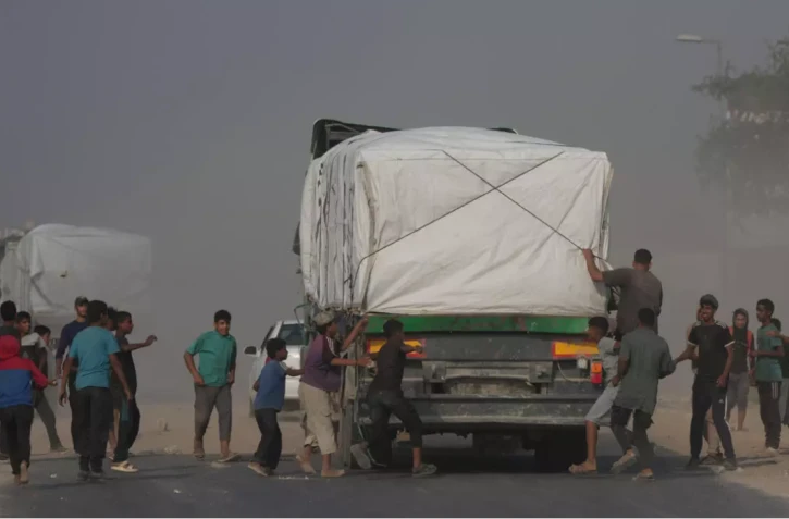 Des Palestiniens se précipitent vers des camions transportant de l'aide humanitaire alors qu'ils traversent Deir al-Balah, dans le centre de Gaza, le dimanche 9 novembre 2025.