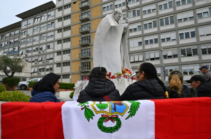 Un drapeau péruvien posé sur un banc où prient des personnes devant la statue de Jean-Paul II, à l'extérieur de l'hôpital Gemelli à Rome, où le pape François est soigné pour une pneumonie