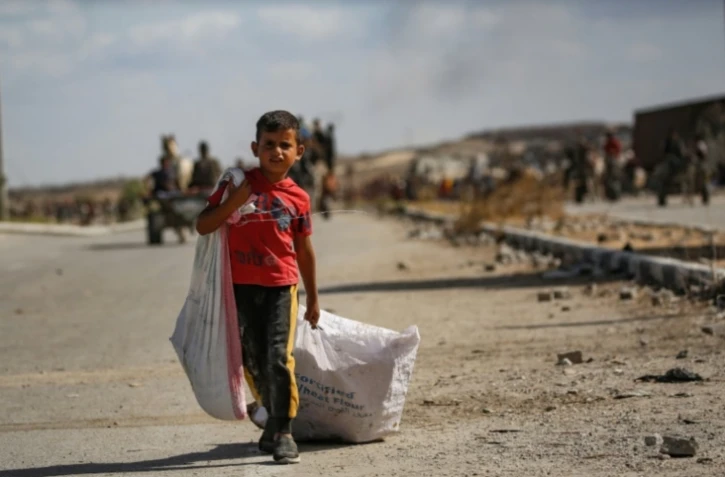 Un garçon palestinien porte un sac et traîne un autre derrière lui alors qu'il revient d'un point de distribution alimentaire dans le centre de la bande de Gaza, le 5 octobre 2025 ( AFP / Eyad BABA )