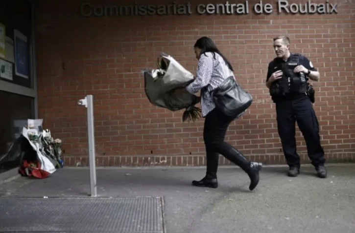 Une femme dépose des fleurs devant le commissariat de Roubaix en hommage aux trois policiers morts la veille dans un accident de la route, le 22 mai 2023 dans le Nord ( AFP / Sameer Al-Doumy )