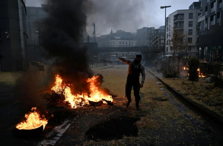 Un manifestant se tient debout près d'un feu de paille et de pneus à Bruxelles le 26 février 2024 (  )