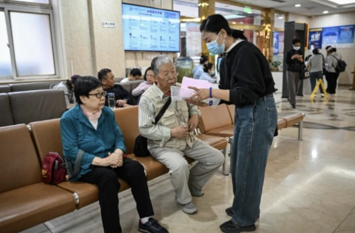 Meng Jia (d), une accompagnatrice de patient, prend en charge Gao Yingmin (g) et Tian Yigui (c) pour les guider dans un hôpital à Pékin, le 22 mai 2025 ( AFP / Jade GAO )