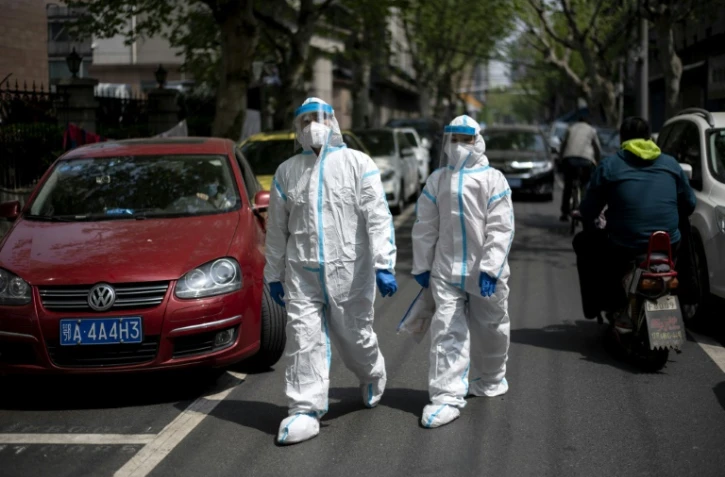 Des habitants en combinaison intégrale de protection dans une rue de Wuhan, le 7 avril 2020 dans la province chinoise du Hubei