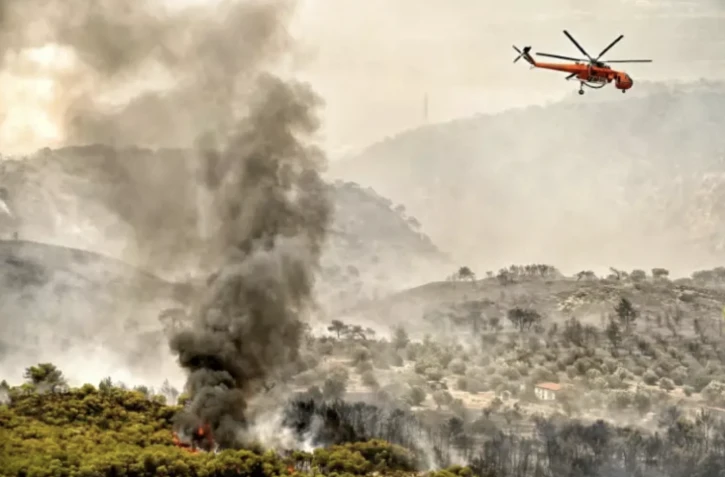 Un hélicoptère largue une cargaison d'eau sur un incendie de forêt à Agioi Theodori, à l'ouest d'Athènes, le 18 juillet 2023 ( AFP / Valerie GACHE )