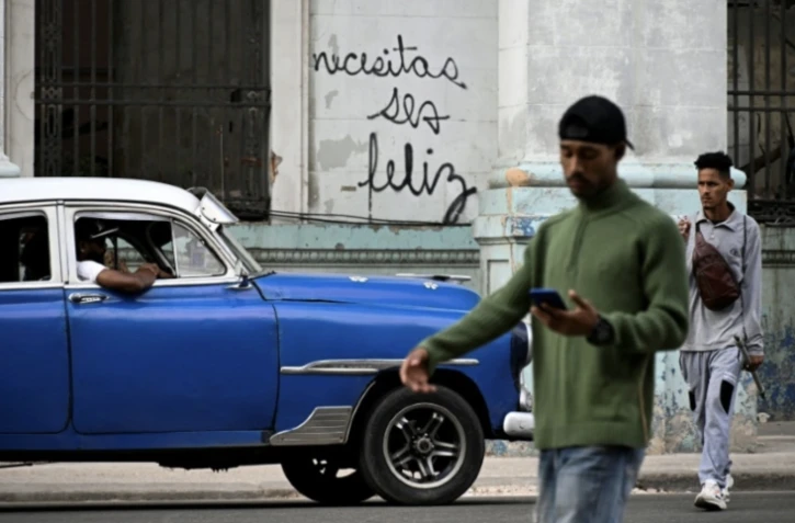 Des Cubains marchent devant le graffiti "Necesitas ser feliz" (Tu dois ĂȘtre heureux) du graffeur cubain Mr. Sad, Ă La Havane, le 12 dĂ©cembre 2024 ( AFP / YAMIL LAGE )