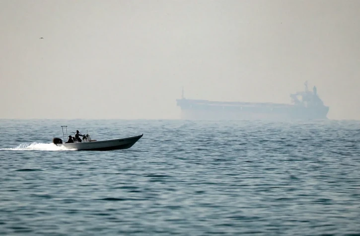 Un bateau à moteur longe la côte au large de la ville d'Al Jeer, sur le détroit d'Ormuz, dans l'émirat de Ras Al Khaimah (nord), avec un pétrolier visible en arrière-plan, le 25 février 2026. - Photo de FADEL SENNA
