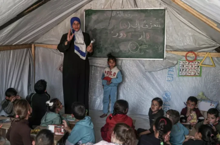 Une enseignante fait un cours à ses élèves le 27 mars 2024 dans une tente d'un camp de déplacés palestiniens à Rafah, dans le sud de la bande de Gaza, où une guerre oppose Israël au mouvement islamiste Hamas ( AFP / SAID KHATIB )