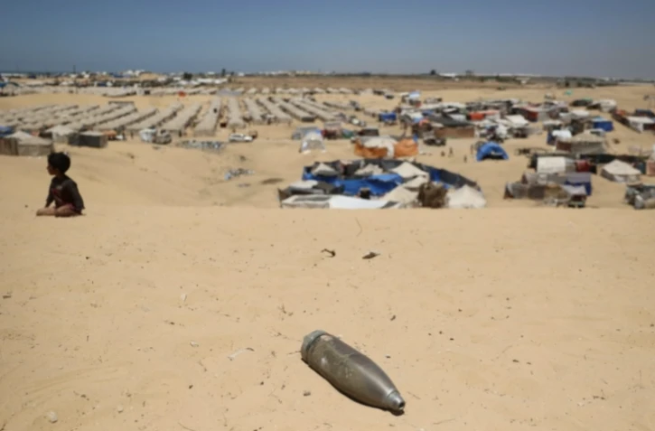 Un obus non explosé non loin d'un enfant assis sur le sable près d'un camp de fortune pour Palestiniens déplacés dans la zone de Tel al-Sultan à Rafah, dans le sud de la bande de Gaza, le 30 mai 2024 ( AFP / Eyad BABA )