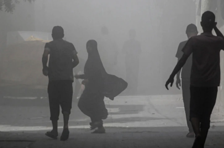 Des Palestiniens marchent dans la fumée et la poussière au camp de Nousseirat, dans le centre de la bande de Gaza, le 8 juin 2024