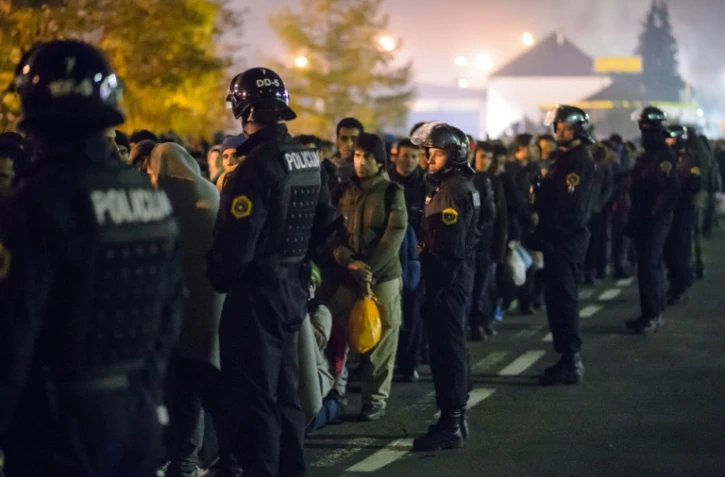 Des policiers slovènes encadrent les migrants sur le point de monter dans un bus le 28 octobre 2015 à Sentilj 