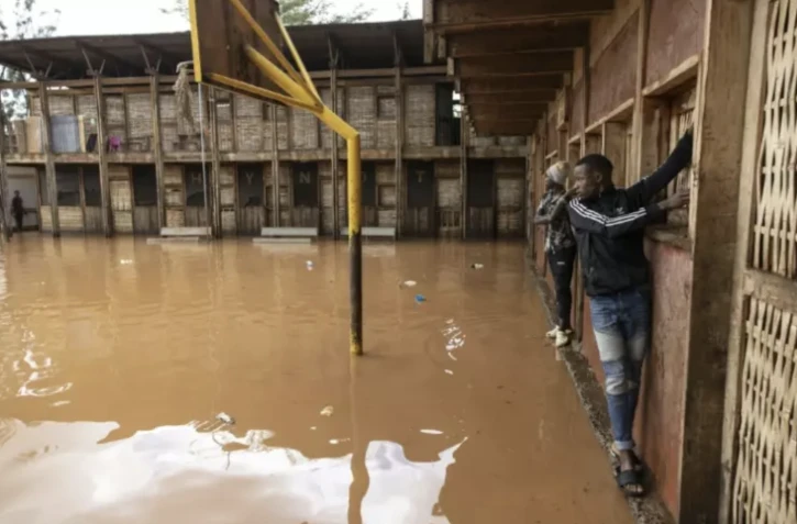 Des habitants du bidonville de Mathare s'accrochent aux murs pour traverser une cour d'école inondée, à Nairobi le 24 avril 2024 ( AFP / SIMON MAINA )