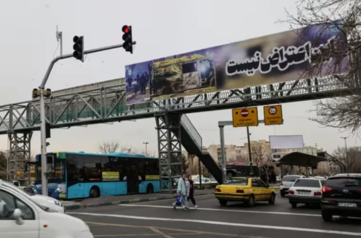 Scène de rue à Téhéran, où une bannière montrant une voiture brûlée proclame "Ceci n'est pas une protestation", le 15 janvier 2026 ( AFP / ATTA KENARE )