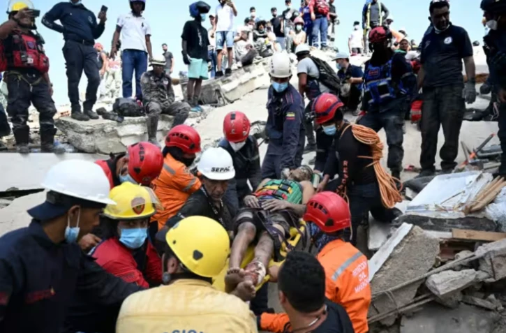 Des membres de la protection civile vénézuélienne et des pompiers sortent un jeune homme des décombres d'un immeuble effondré à Catia La Mar, dans l'Etat de La Guaira, au Venezuela, le 26 juin 2026 ( AFP / Federico PARRA )