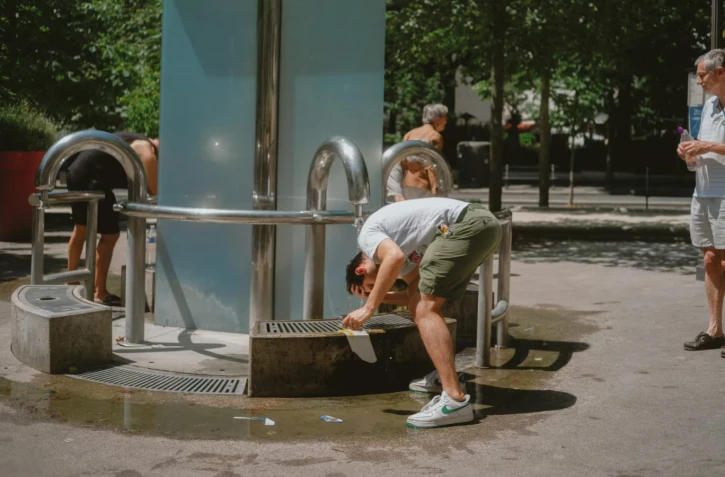 Des parisiens se rafraichissent et remplissent leurs bouteilles d'eau à la fontaine de la Butte aux Cailles, le 21 juin 2026. (JUDITH CRICO / HANS LUCAS / AFP)
