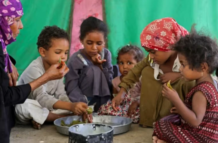 Saeedah Mohammed, une déplacée yéménite, nourrit ses petits-enfants avec des feuilles bouillies dans leur tente du camp d'Al-Manij, près de Taëz, dans le sud ouest du Yémen, le 21 mai 2026 ( AFP / Ahmed al-Basha )