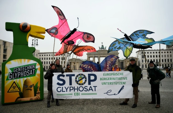 Des environnementalistes brandissent des maquettes de papillons géants à côté d'un immense spray de désherbant au glyphosate devant la porte de Brandebourg à Berlin, le 8 février 2017