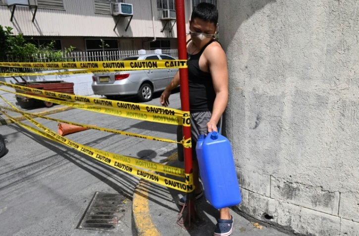 Un homme masqué, un bidon d'eau à la main, franchit la limite d'une rue confinée pour cause de Covid-19 à Manille, le 10 mars 2021