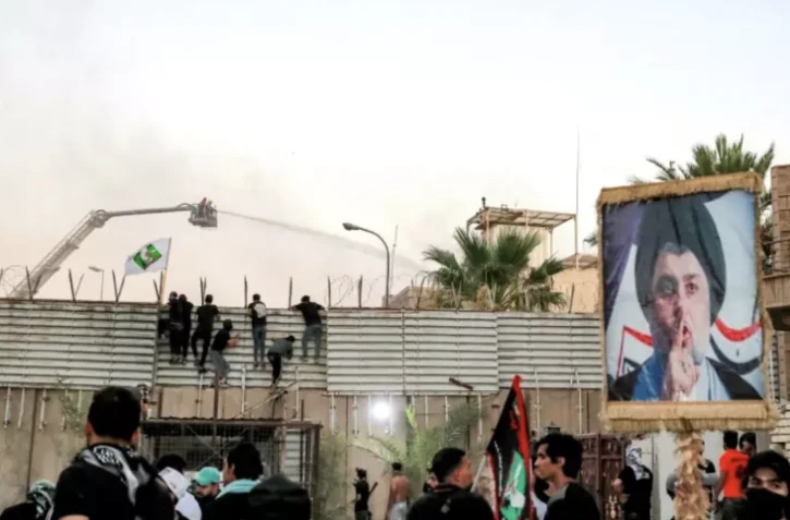 Des soutien du leader religieux chiite Moqtada Sadr, dont l'effigie s'affiche sur un panneau (d), essaient d'escalader la barrière devant l'ambassade de Suède à Bagdad, le 20 juillet 2023 ( AFP / Ahmad AL-RUBAYE )