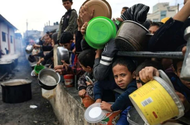 Des Palestiniens attendent avec des récipients pour recevoir de la nourriture dans un camp de réfugiés à Rafah, dans le sud de la bande de Gaza, le 23 décembre 2023