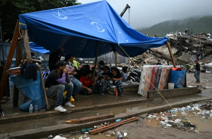 Des rescapés du double séisme s’abritent sous une bâche tandis que les secouristes fouillent les décombres des immeubles effondrés à Caraballeda, dans l’État de La Guaira, au Venezuela, le 11 juillet 2026