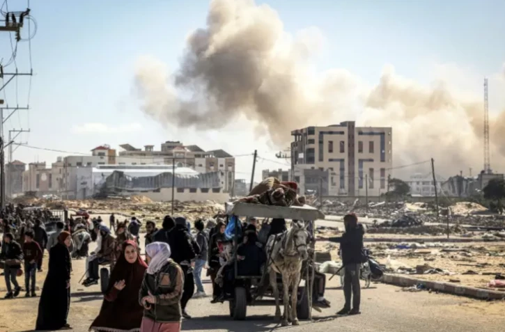 Des Palestiniens fuient Khan Younès dans le sud de la bande de Gaza, avec en arrière-plan un nuage de fumée s'élevant après des bombardements, le 30 janvier 2024 ( AFP / Mahmud Hams )