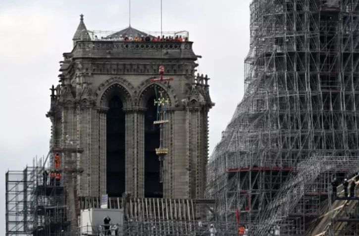 La croix de Notre-Dame de Paris soulevée par une grue pour être placée au sommet de la flèche de la cathédrale, le 6 décembre 2023, à Paris ( AFP / Miguel MEDINA )