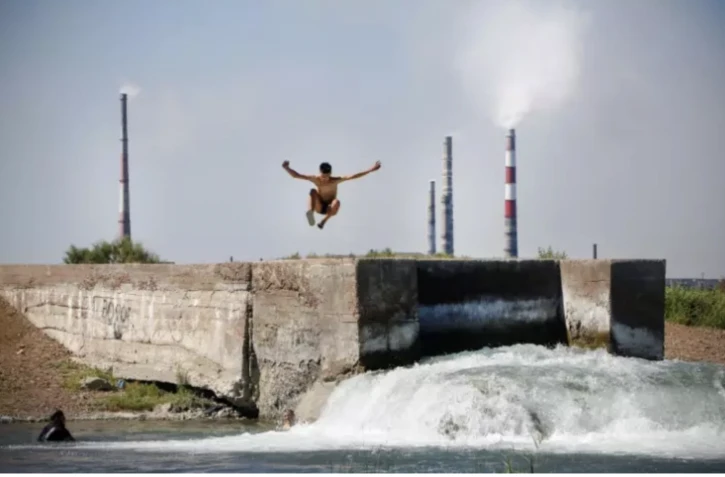 Un adolescent plonge dans de l'eau rejetée par le complexe métallurgique de Kazakhmys à Balkhach au Kazakhstan, le 20 juin 2024 ( AFP / Ruslan PRYANIKOV )