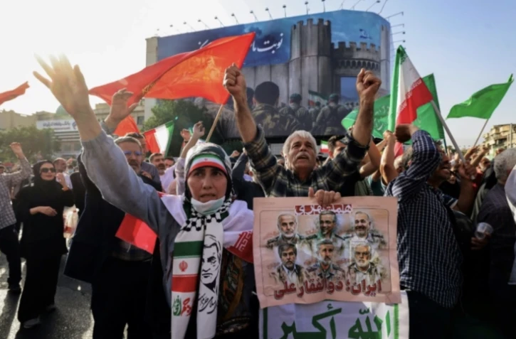Des Iraniens brandissent des drapeaux et des pancartes lors d'un rassemblement de protestation contre l'attaque américaine en Iran sur la place Enghelab à Téhéran, le 22 juin 2025 ( AFP / ATTA KENARE )