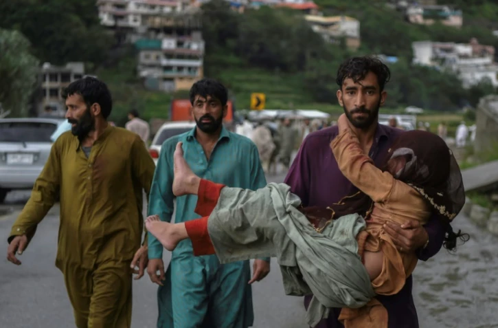 Un homme porte sa fille malade le long d'une route endommagée par les eaux de crue suite aux fortes pluies de mousson dans la région de Madian, dans la vallée de Swat, au nord du Pakistan, le 27 août 2022