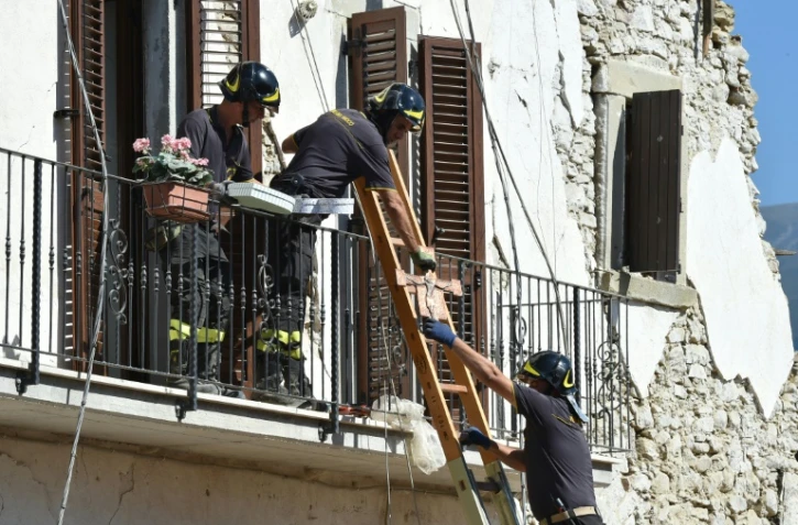 Des pompiers aident les habitants à récupérer leurs affaires personnelles dans les maisons endommagées par le séisme, le 28 août 2016 à Amatrice, dans le centre de l'Italie