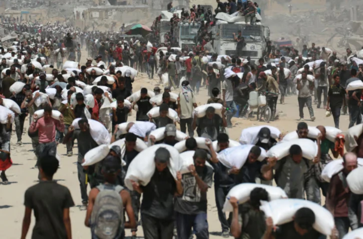 Des Palestiniens transportent des sacs de farine près de Jabalia, le 27 juillet 2025, après que des camions transportant de l'aide humanitaire sont entrés dans le nord de la bande de Gaza.  AFP - AFP or licensors - BASHAR TALEB