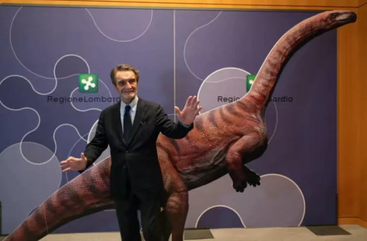 Attilio Fontana, président de la région italienne de Lombardie, pose pour une photo avec un dinosaure en carton lors d'une conférence de presse pour présenter la découverte de milliers d'empreintes de dinosaures dans le parc national du Stelvio, en Italie, prÚs des zones qui accueilleront les Jeux olympiques d'hiver e Milan-Cortina 2026, à Milan, le 16 décembre 2025. On estime que ces empreintes appartiennent à des dinosaures prosauropodes du Trias supérieur, datant de 210 millions d'années. ( AFP / Piero CRUCIATTI )