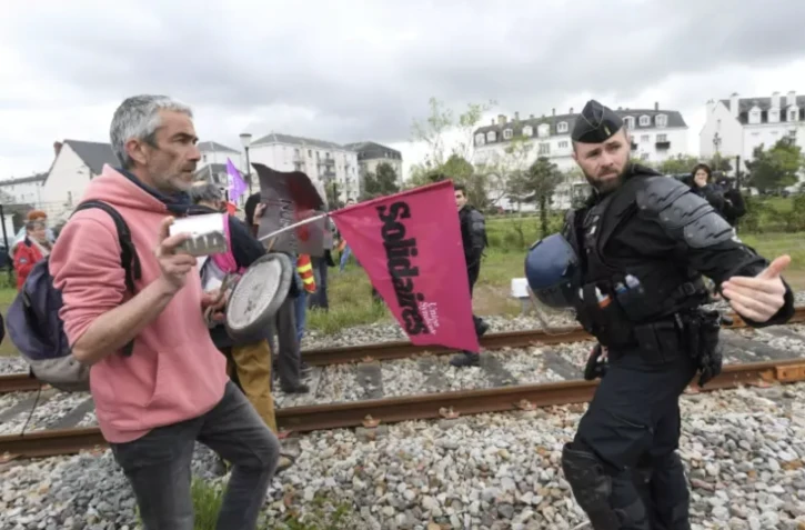 Un policier face à des manifestants rassemblés sur une voie ferrée près de la maison de santé que doit visiter le président Emmanuel Macron, le 25 avril 2023 à Vendôme, dans le Loir-et-Cher ( AFP / JEAN-FRANCOIS MONIER )