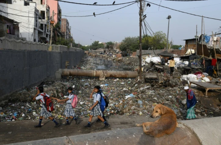 Des écolières passent devant un canal d'évacuation des égoûts rempli de déchets dans le bidonville Taimur Nagar à New Delhi le 30 mai 2018