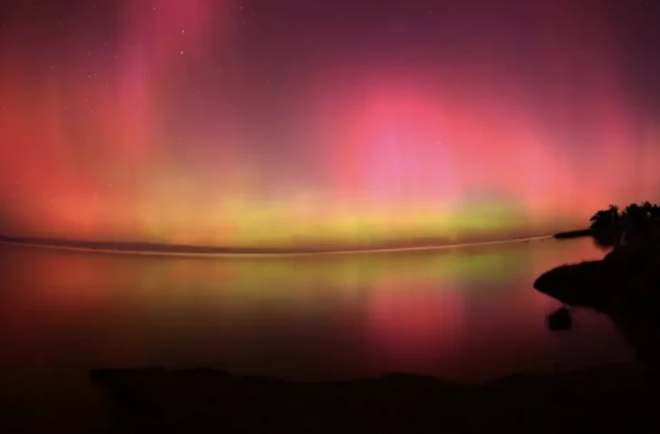 Une aurore australe vue au dessus des eaux du lac Ellesmere, près de Christchurch en Nouvelle Zélande le 11 mai 2024 ( AFP / Sanka Vidanagama )