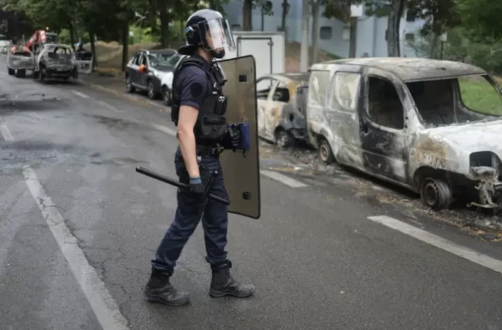 Un policier à proximité de véhicules calcinés après une quatrième nuit consécutive d'émeutes causées par la mort de Nahel, le 1er juillet 2023 à Nanterre ( AFP / CHARLY TRIBALLEAU )