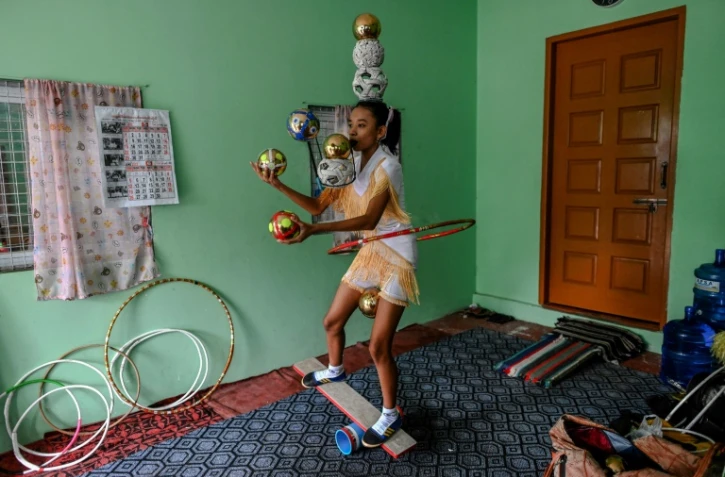 Han Myint Mo tient en équilibre une balle dorée sur la lame d'un couteau, le manche entre ses dents, lors d'un entraînement de jonglage, le 5 juillet 2022 à Rangoun, en Birmanie